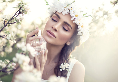 Kobieta z wiankiem w brązowych włosach na tle kwiatów wącha perfumy Kobieta z wiankiem w brązowych włosach na tle kwiatów wącha perfumy