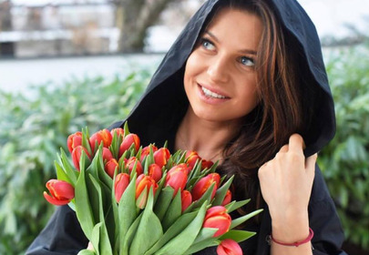 Anna Lewandowska w czarnym kapturze trzyma bukiet czerwonych tulipanów z zielonymi łodygami Anna Lewandowska w czarnym kapturze trzyma bukiet czerwonych tulipanów z zielonymi łodygami